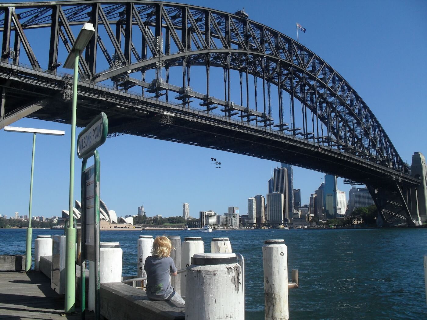 A suspension bridge spanning a river, with a cityscape on the other side.