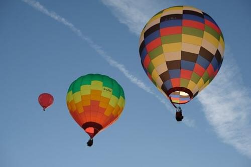 Three hot air balloons against a clear sky, as seen from the ground